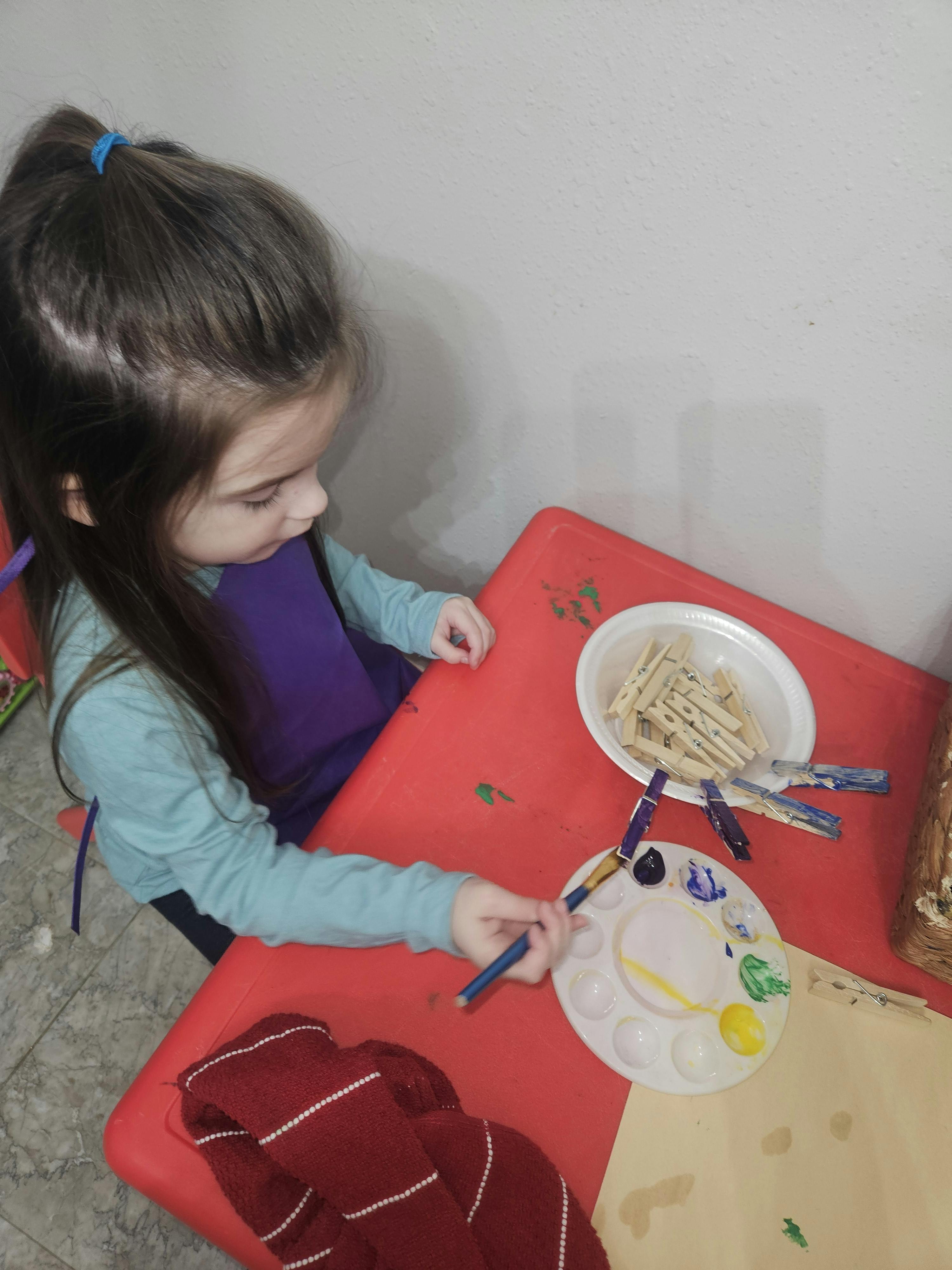 Child painting with a brush and palette at a red table