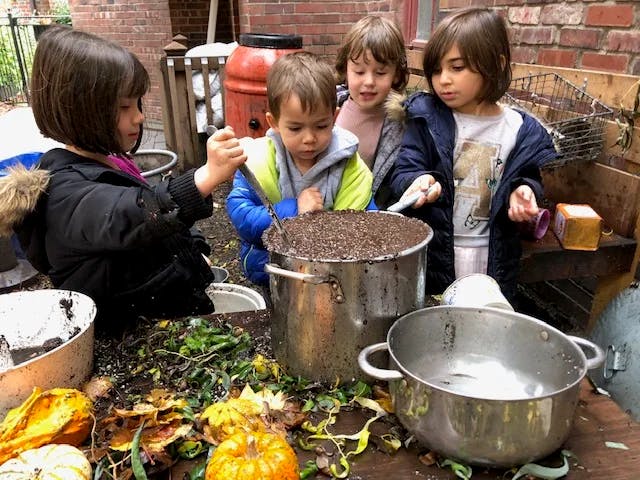 Four children playing with dirt and leaves in large pots outdoors
