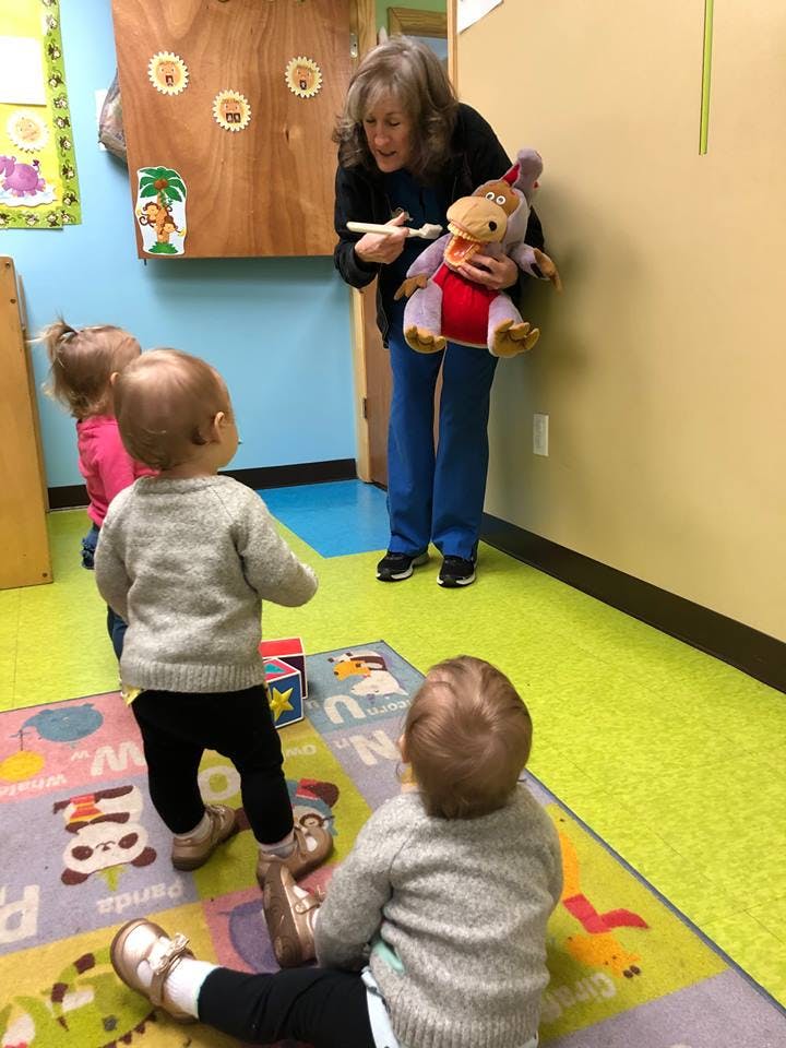 Person holding a stuffed animal and a toothbrush, with children watching