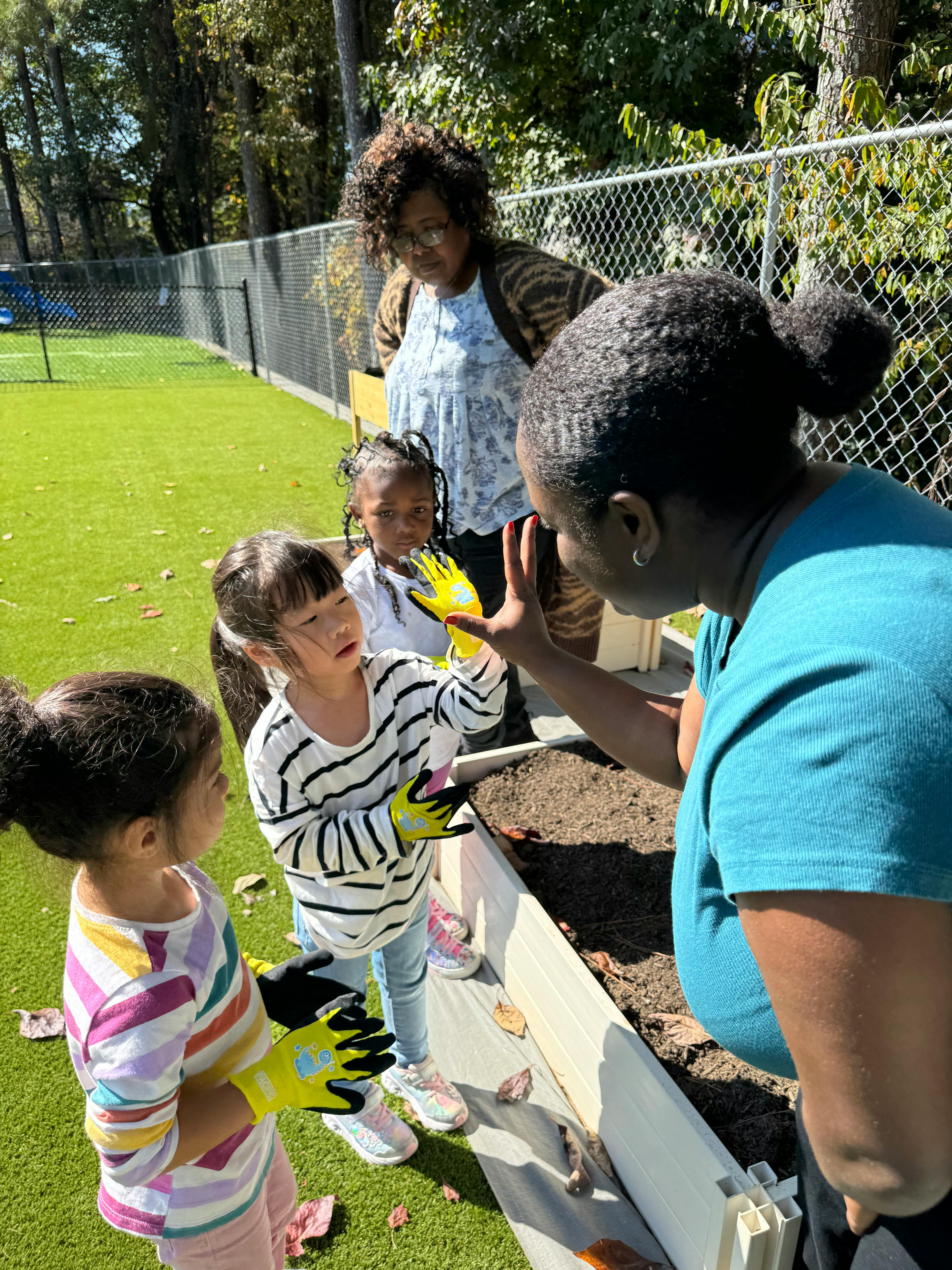 Adults and children in gardening gloves around a raised garden bed