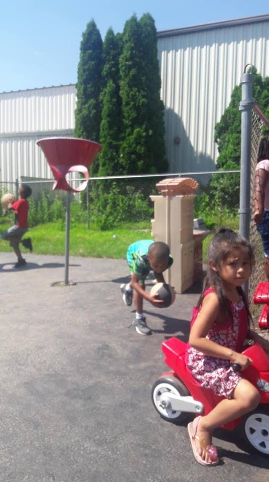 Children playing outdoors, one on a red ride-on toy, others with basketballs