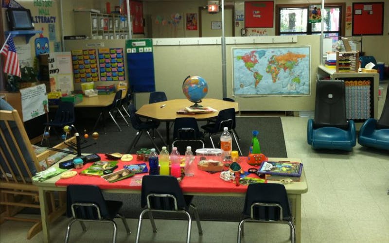 An empty classroom with multiple tables, chairs, and learning materials