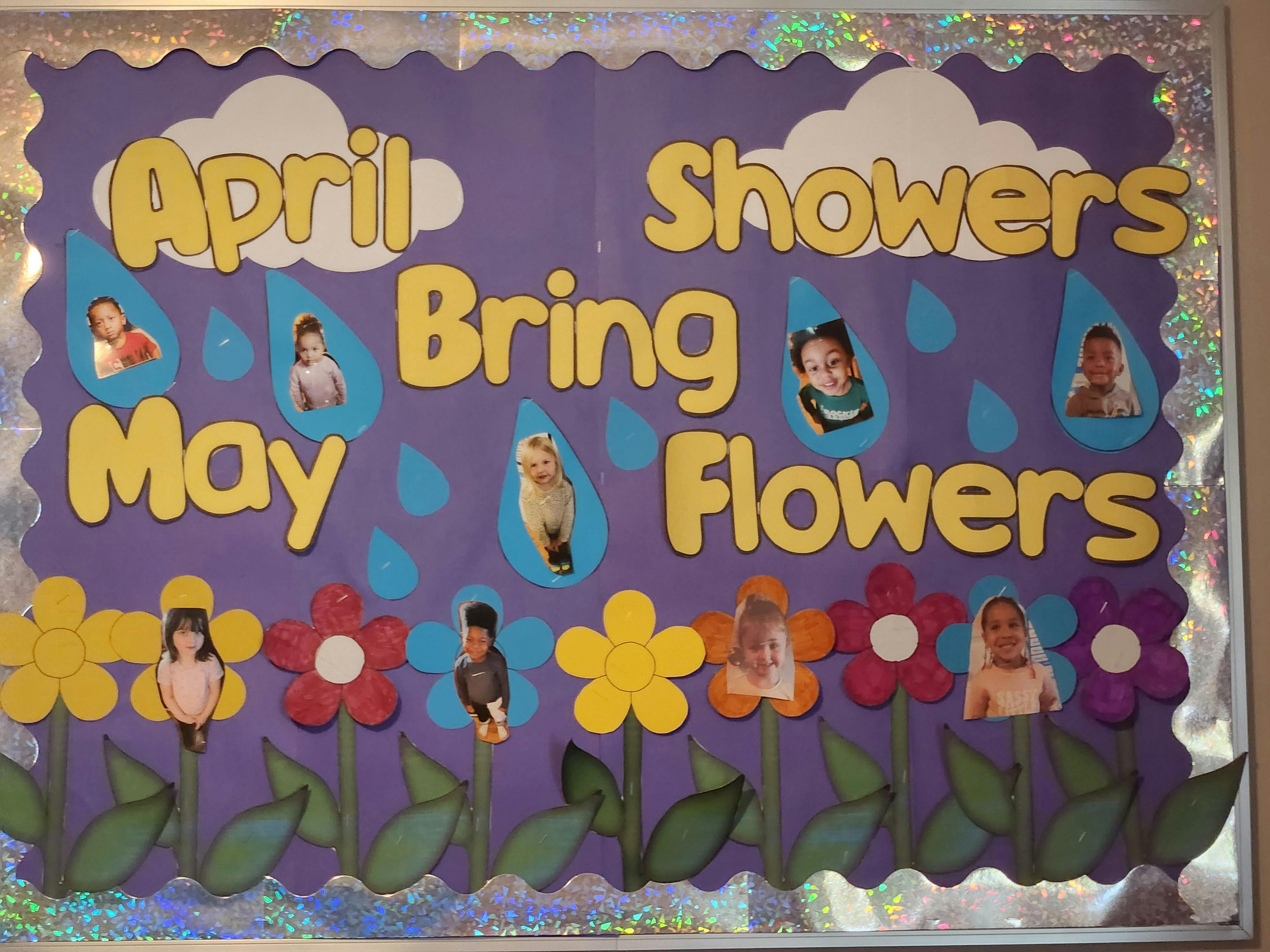 Bulletin board with "April Showers Bring May Flowers" and child photos