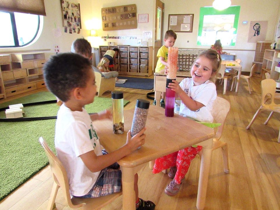 Two children playing with sensory bottles at a table in a classroom