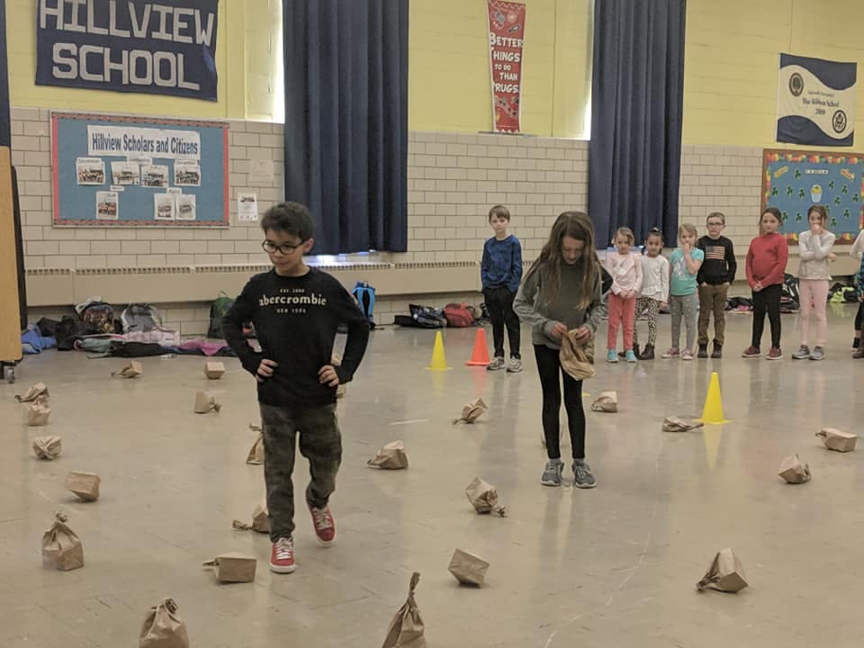 Children in a gym with paper bags on the floor