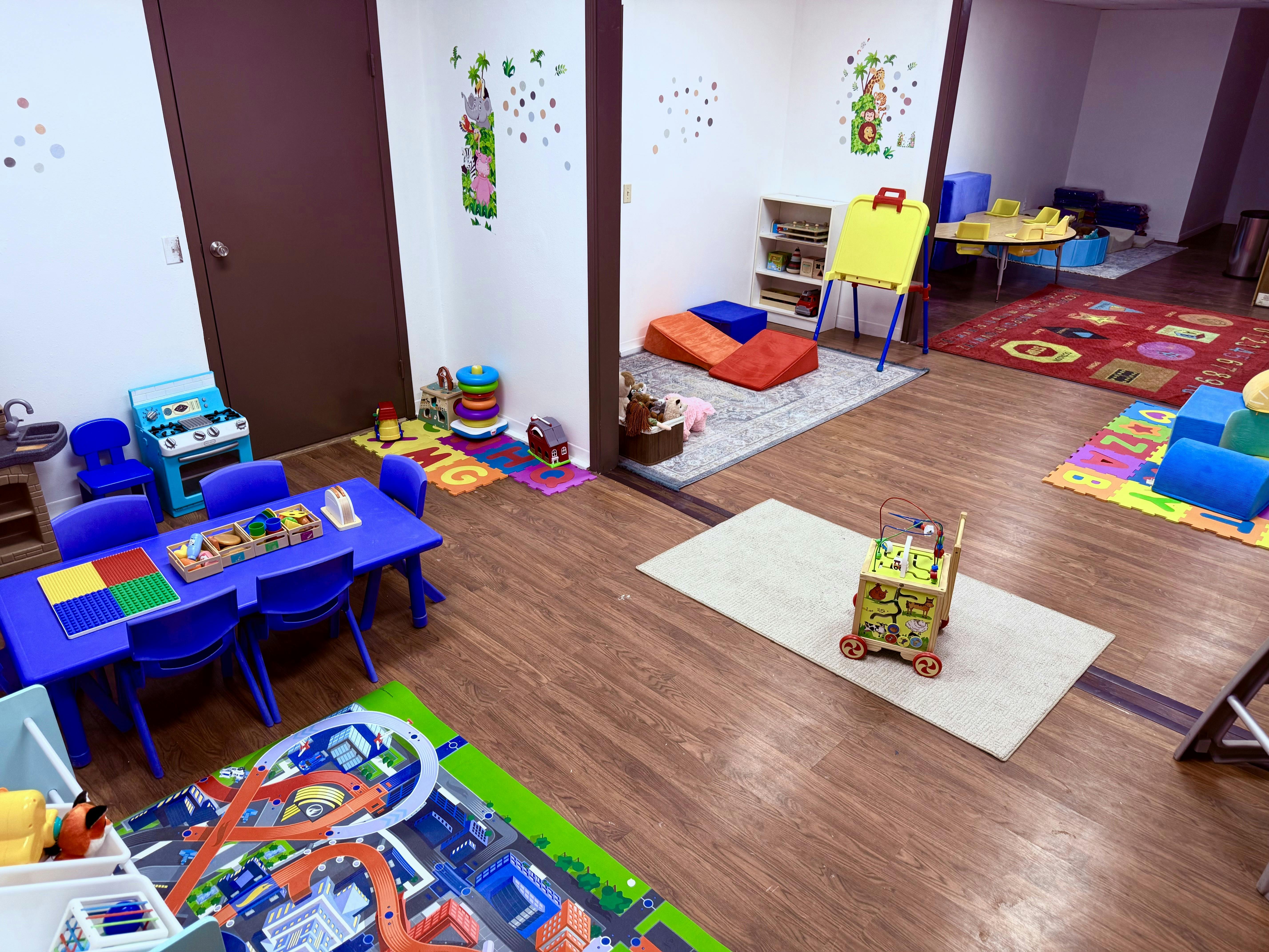 Playroom with blue tables and chairs, toy kitchen, and colorful rugs