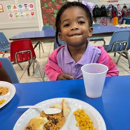 Child sitting at a table with a plate of food and a cup