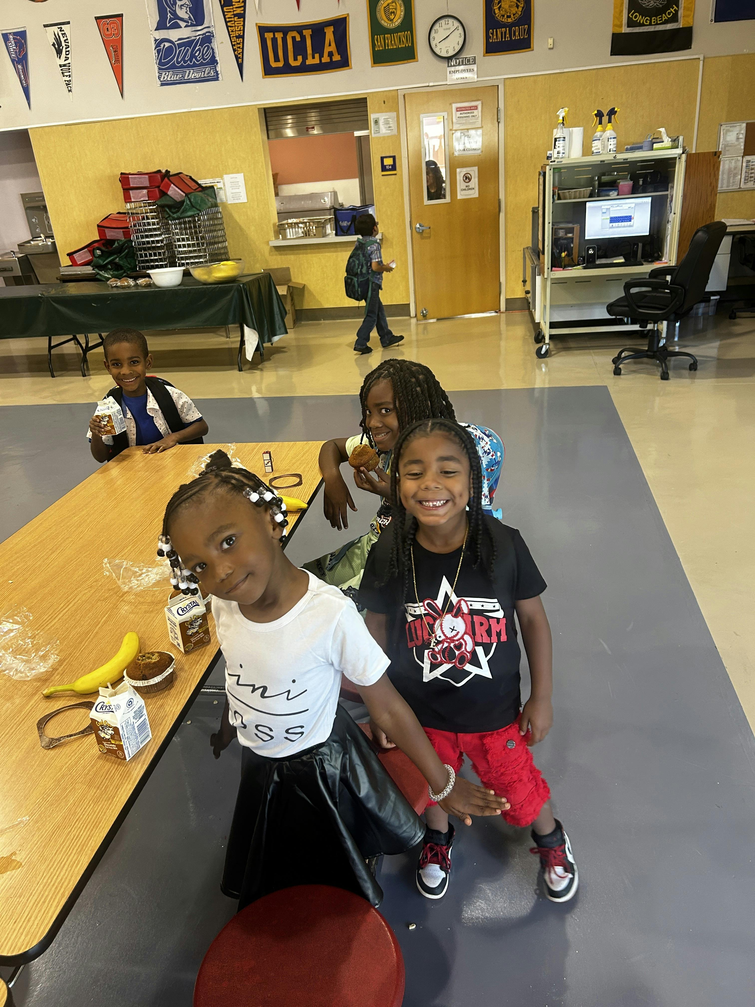 Three children posing for a photo at a table, another child in background