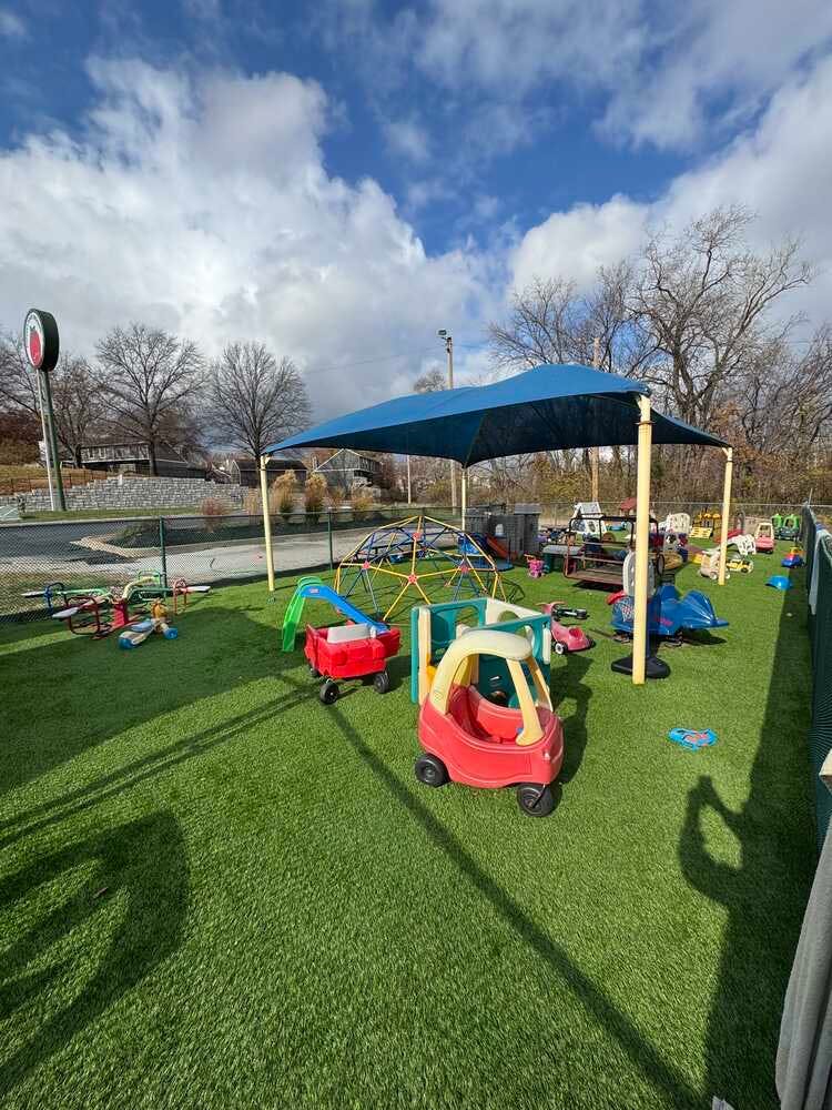 Outdoor playground with artificial turf, play equipment, and a blue shade