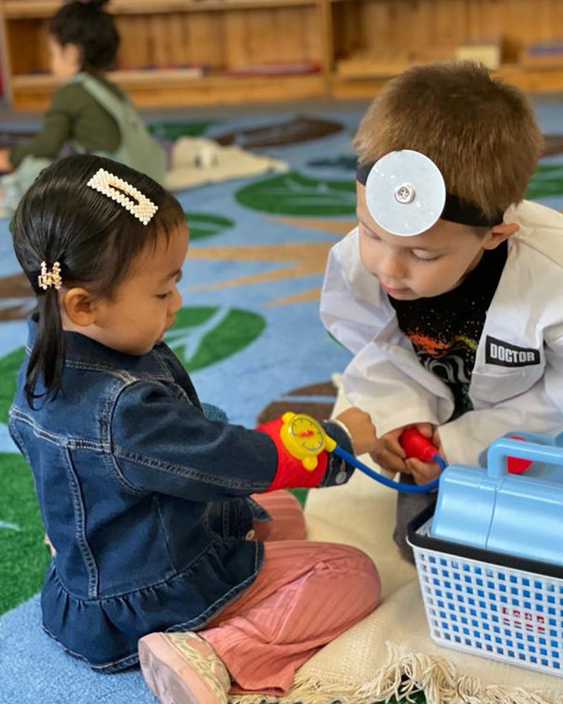 Child in doctor costume checking another child's arm with toy medical equipment
