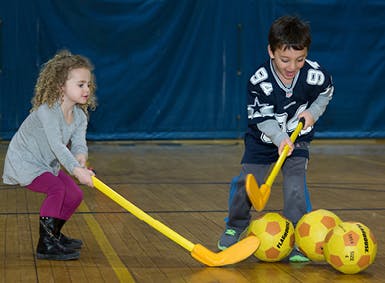 Two children playing floor hockey with yellow sticks and balls