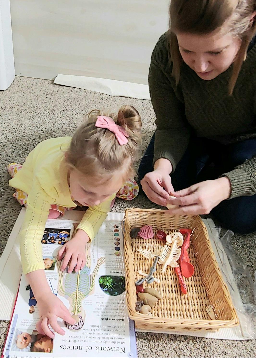 Person and child on floor with book and basket of objects
