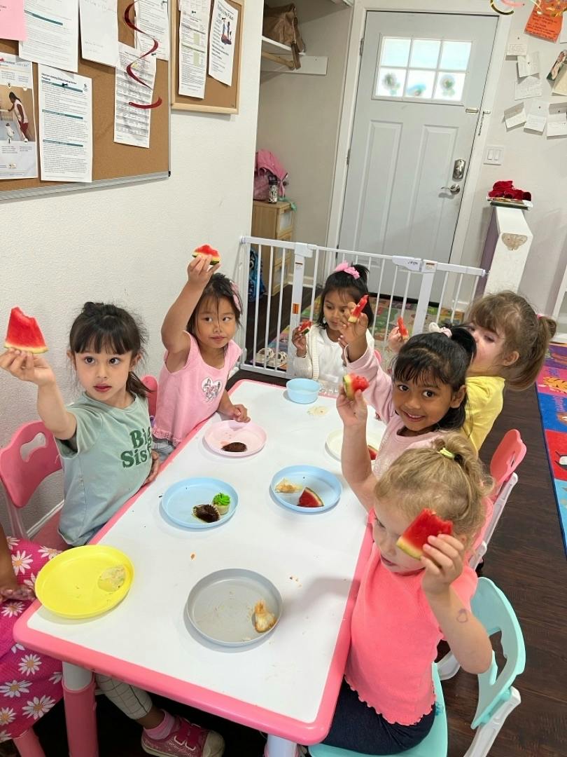 Group of children sitting at a table eating slices of watermelon