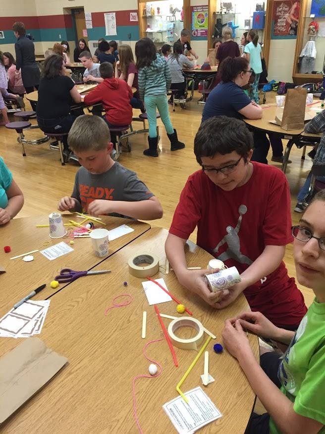 Two children working on a craft project at a table with various supplies on the table