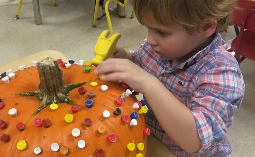 Child decorating a pumpkin with colorful bottle caps