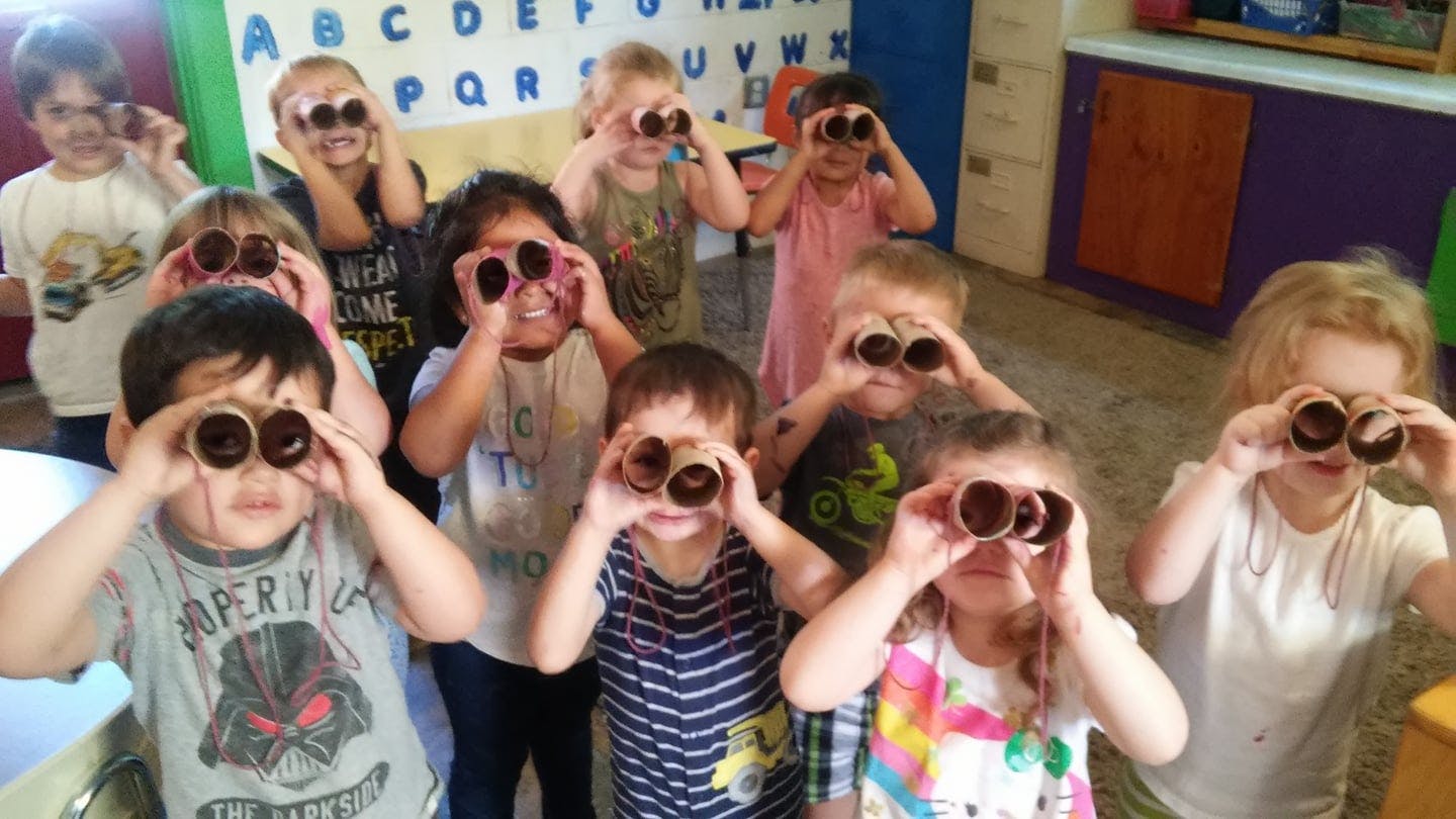 Group of children looking through binoculars in a classroom