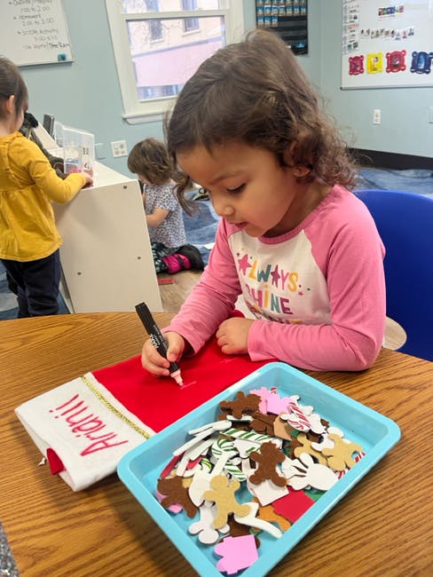 Child drawing on a red fabric with craft cutouts in a tray nearby