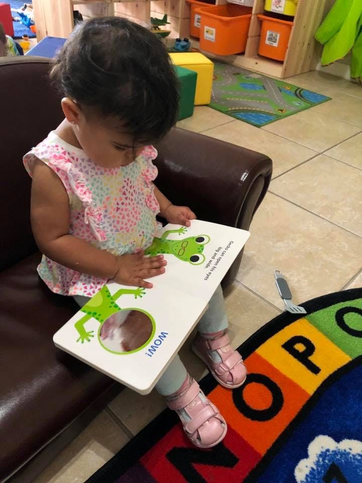 Child sitting on a couch reading a book with a frog on the cover