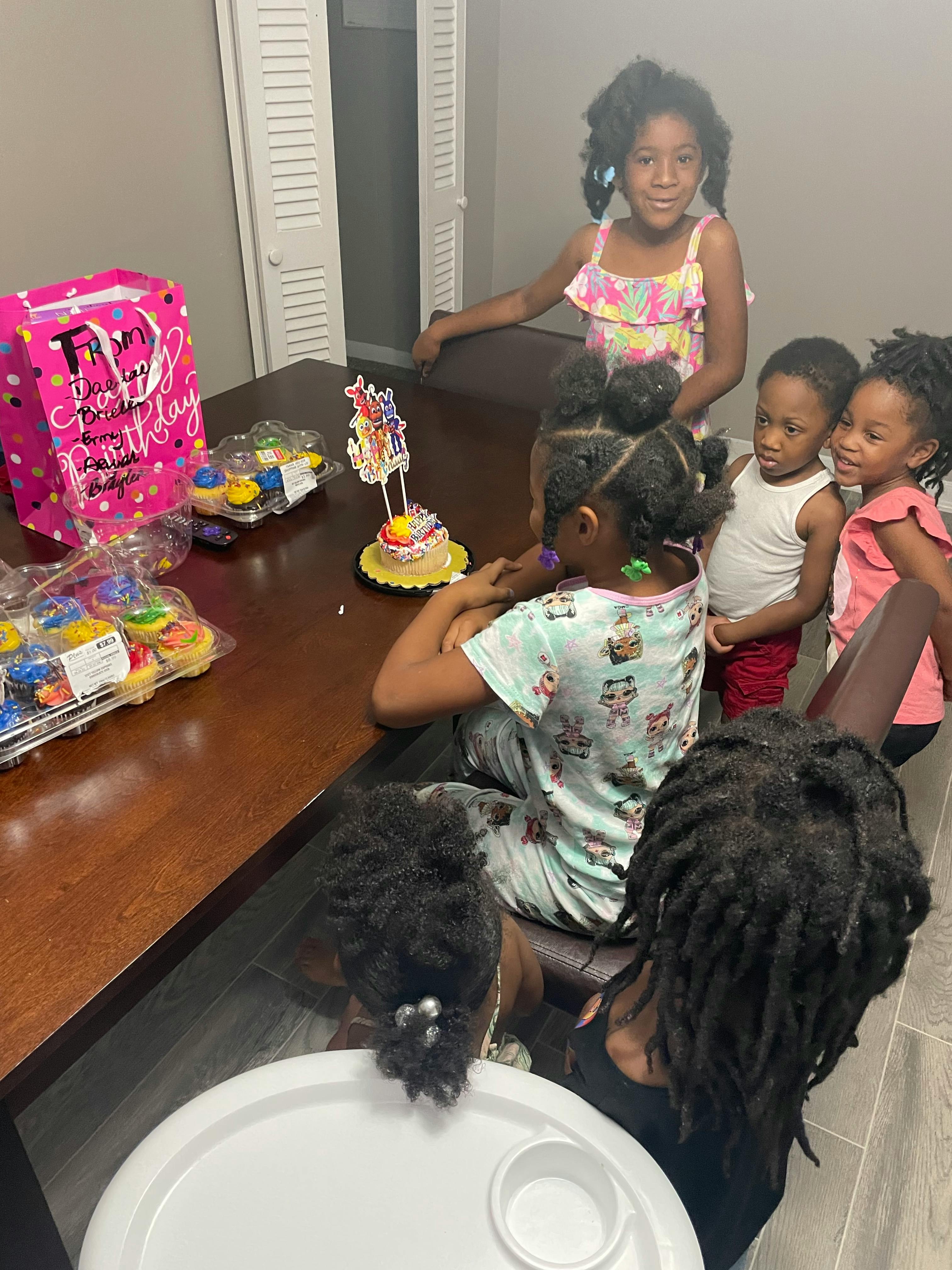 Children gathered around a table with a birthday cake and cupcakes