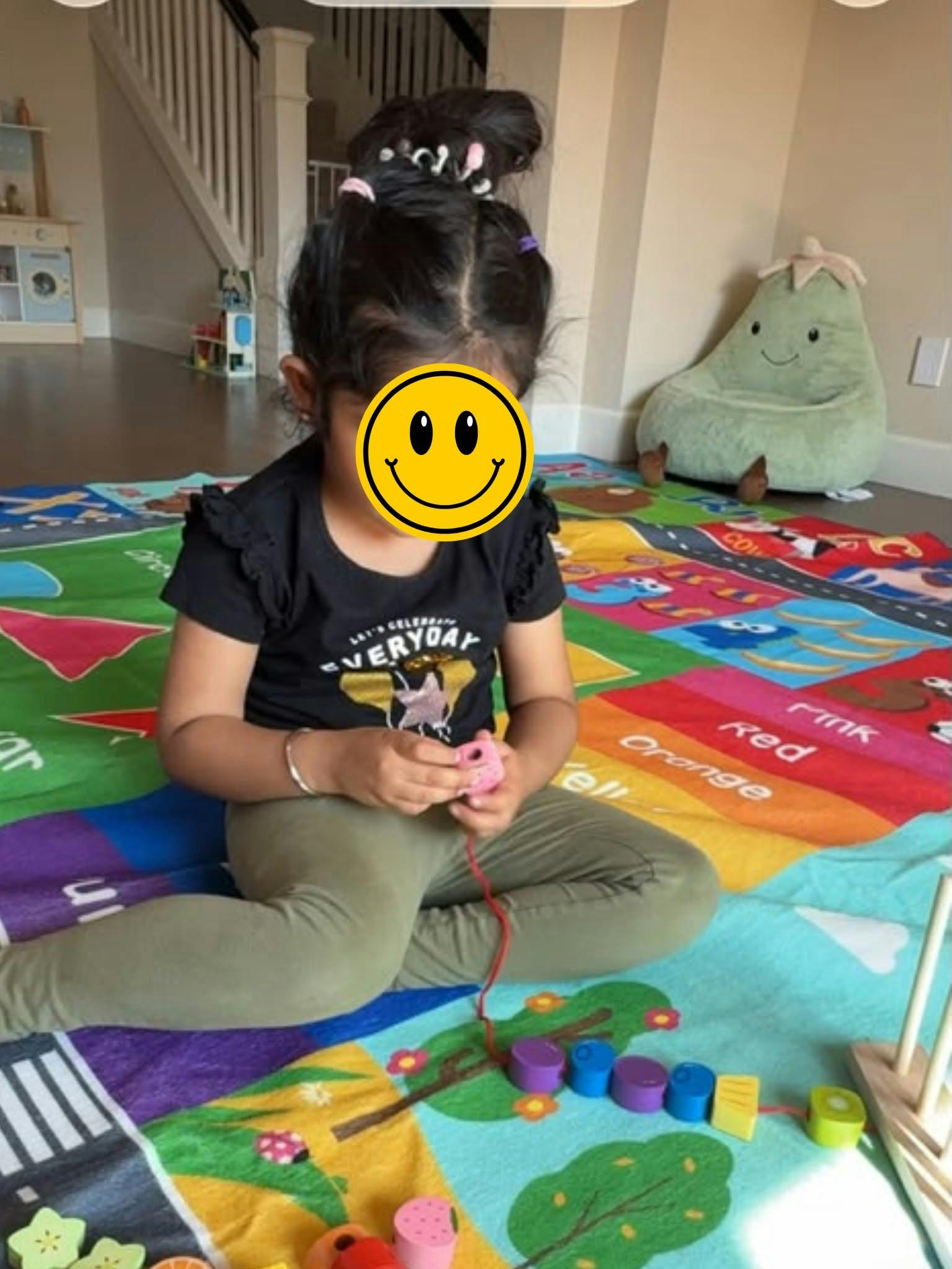 Child sitting on a colorful play mat stringing wooden beads
