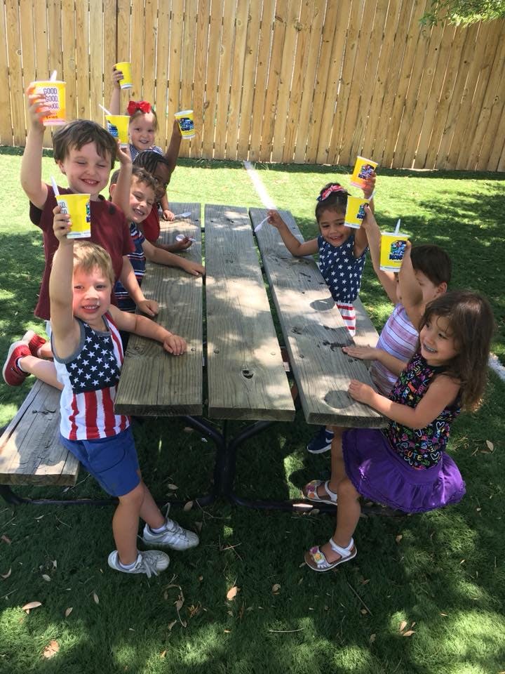 Children sitting at a picnic table holding up cups