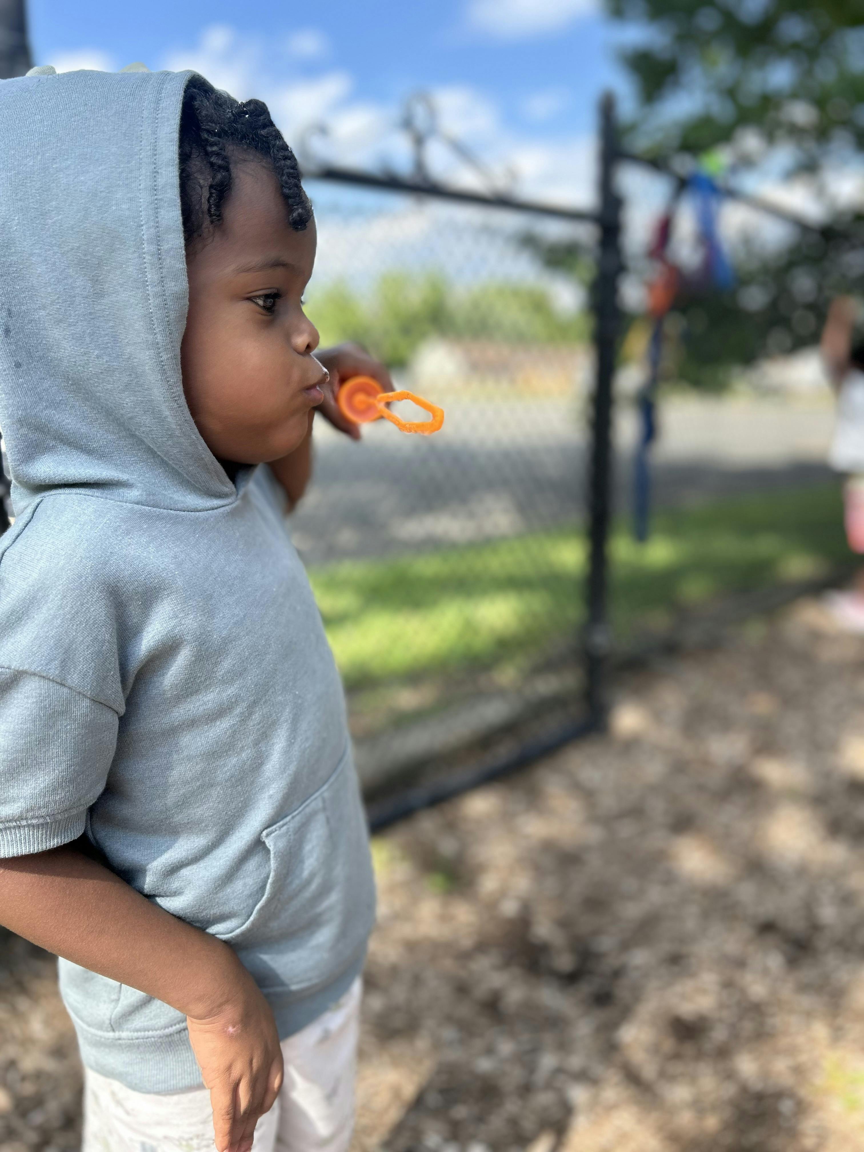 Child in a hooded shirt blowing bubbles with an orange wand