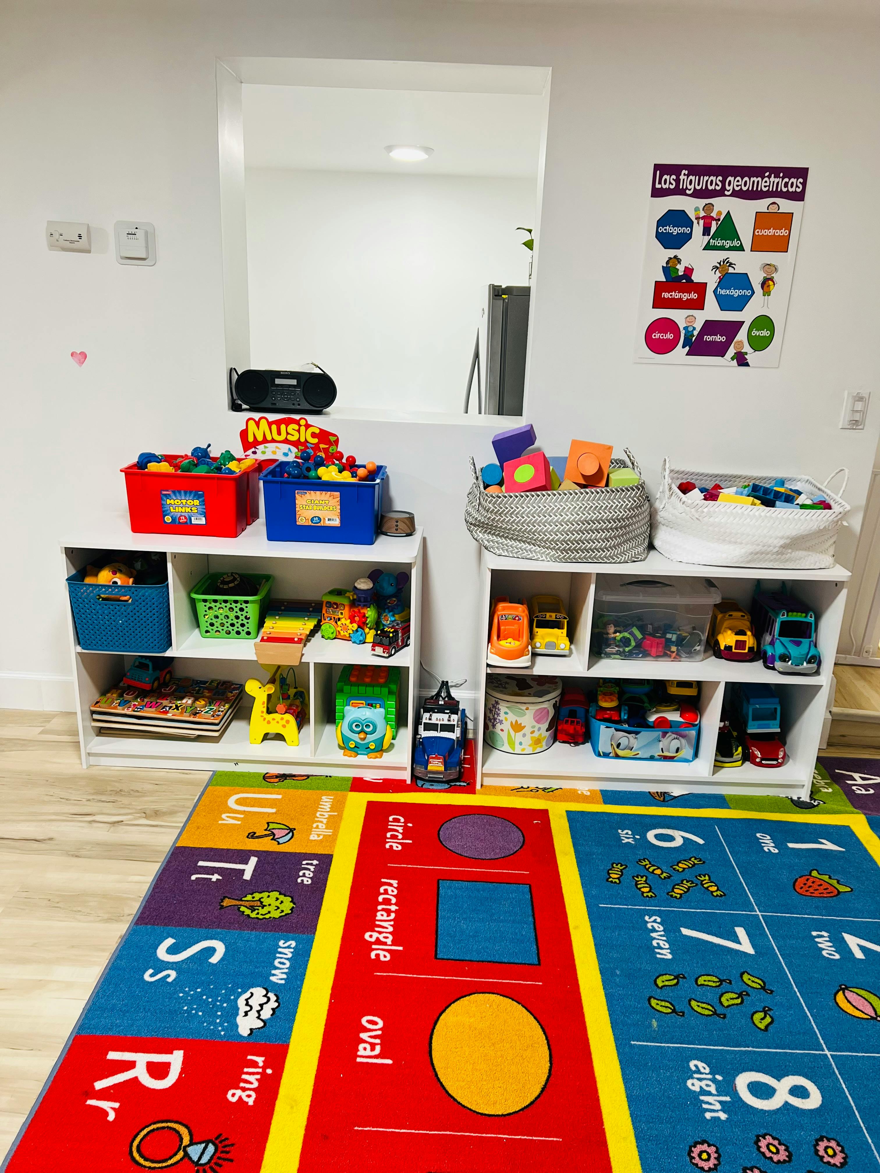Playroom with shelves of toys, a colorful rug, and a geometric shapes poster