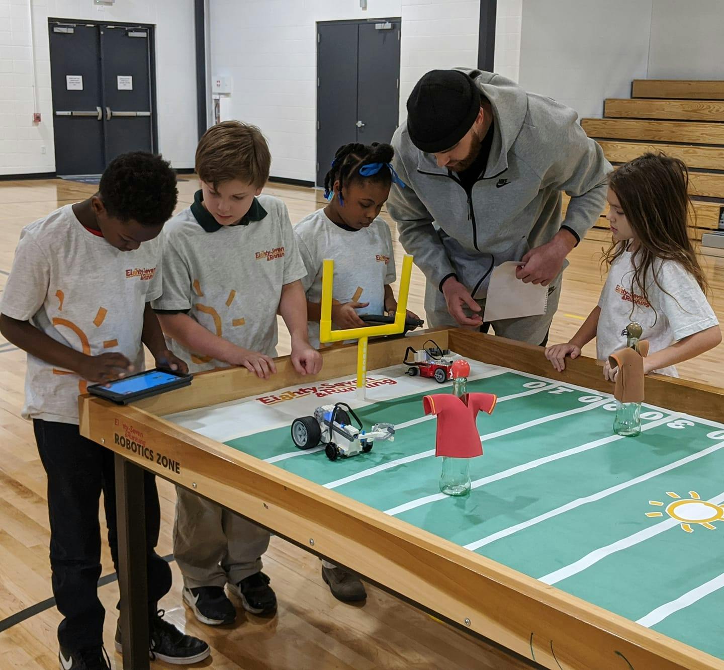 Adult and children gathered around a table with a robot and football field