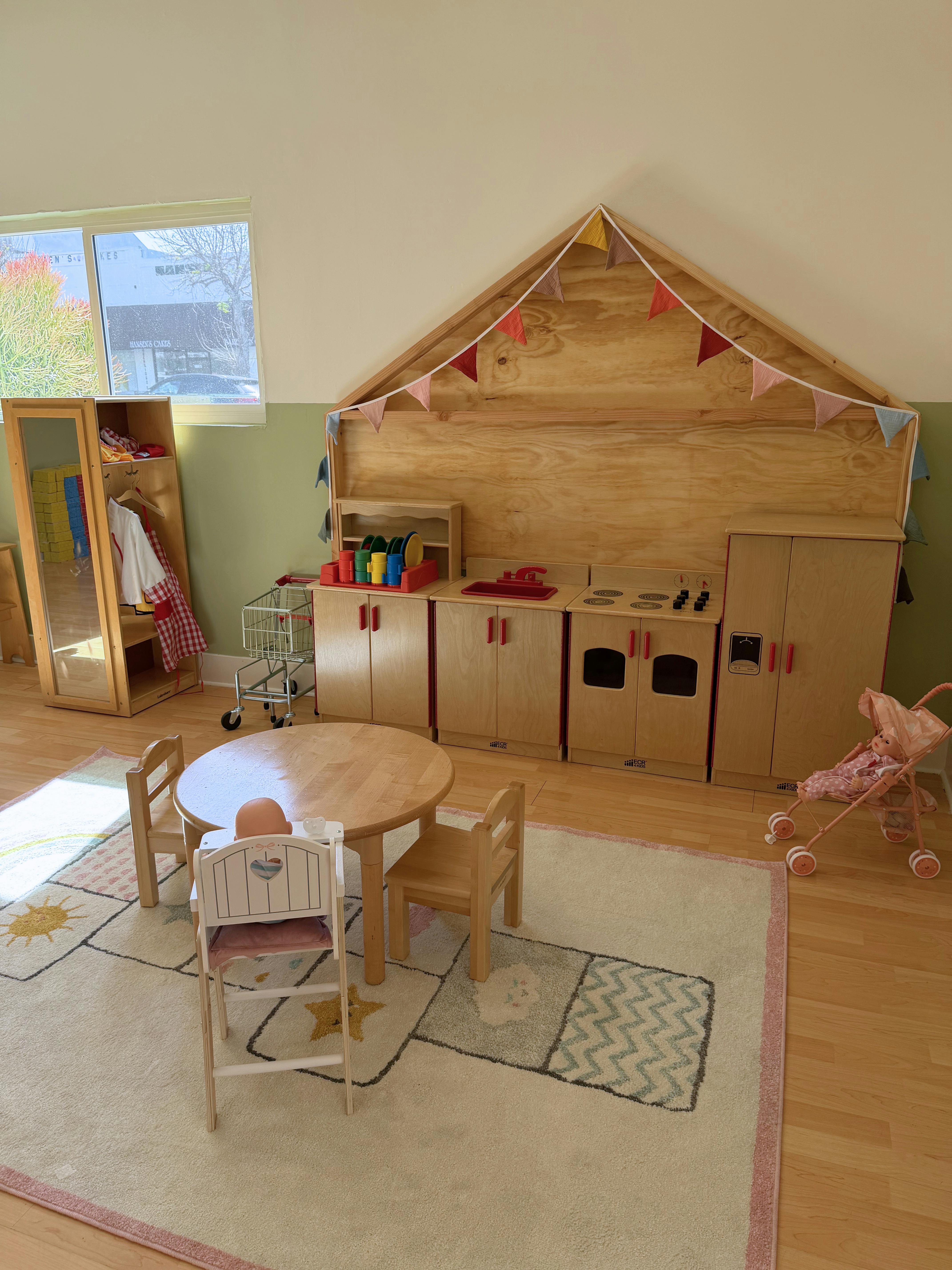 Playroom with doll high chair at a round table and a toy kitchen