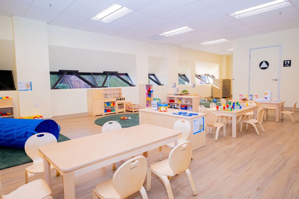 Empty preschool classroom with small tables, chairs, and play areas