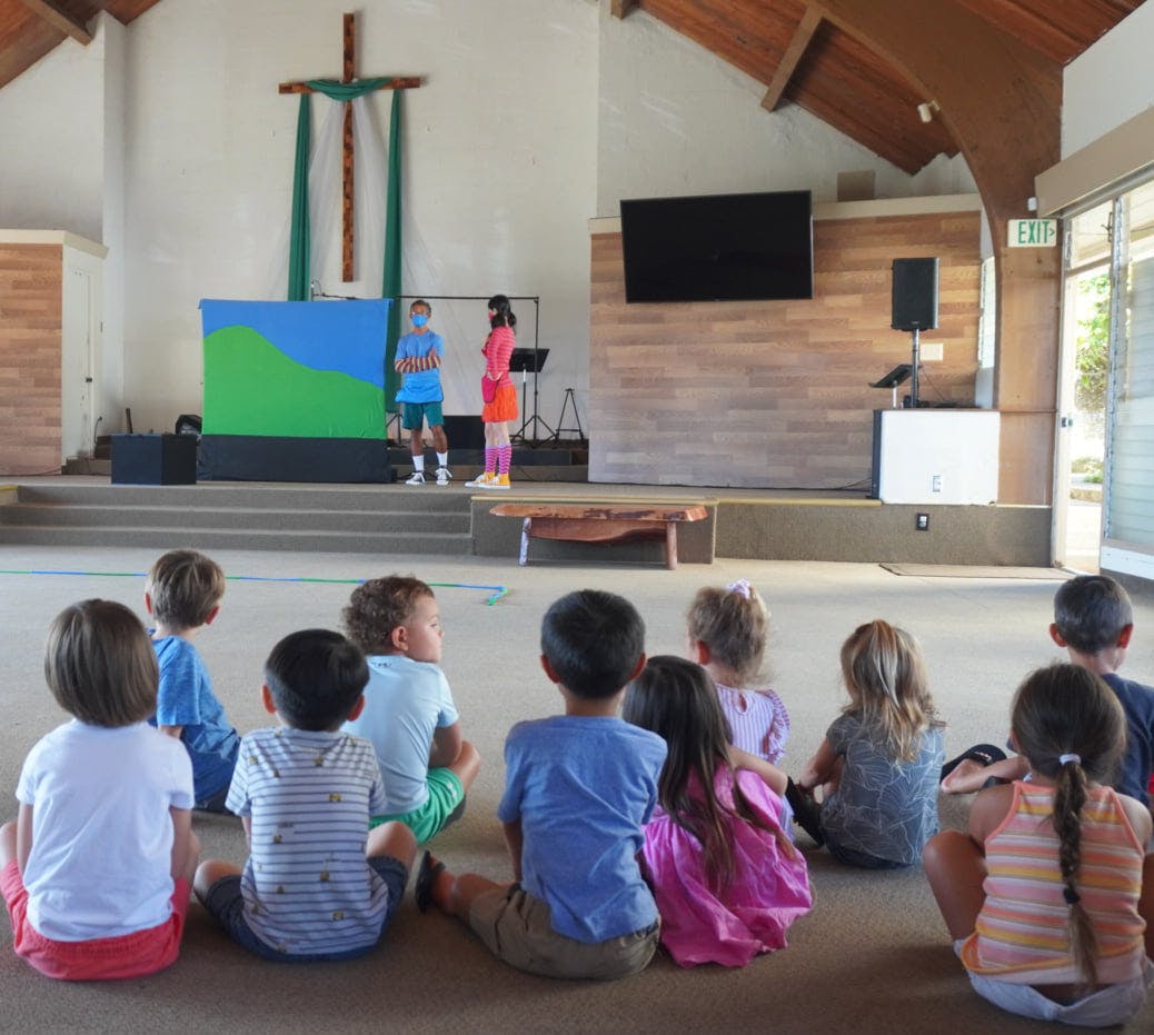 Children sitting on the floor watching people on a stage