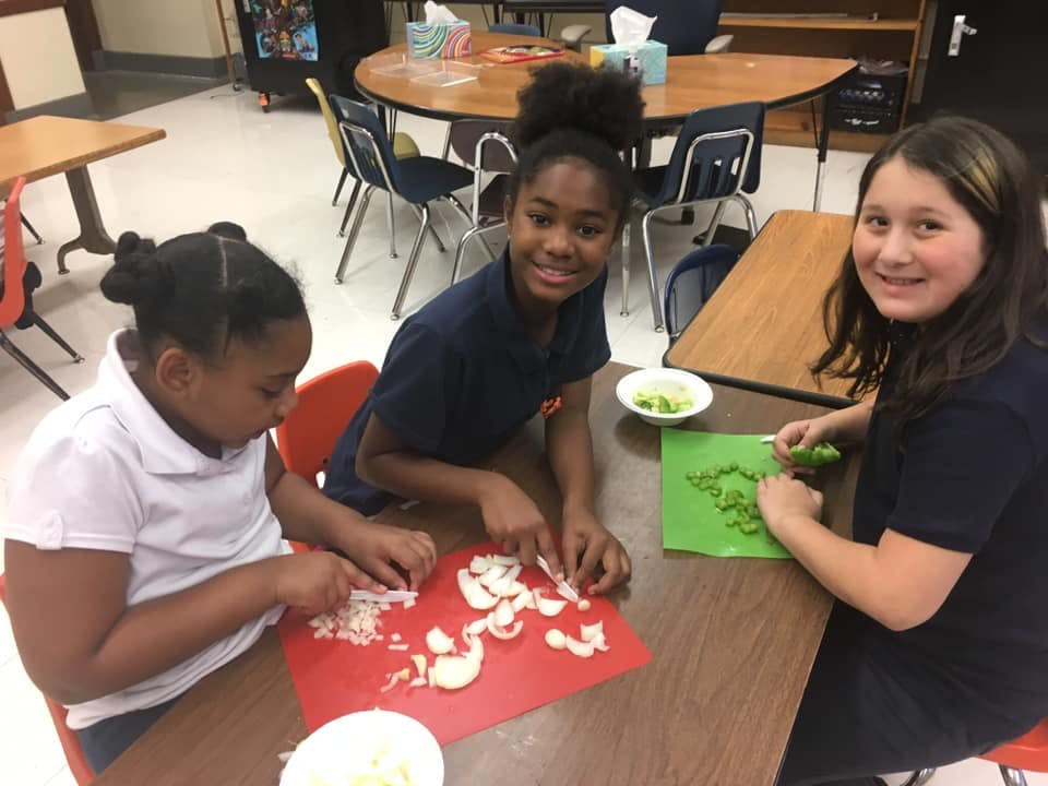 Three children chopping vegetables in a classroom