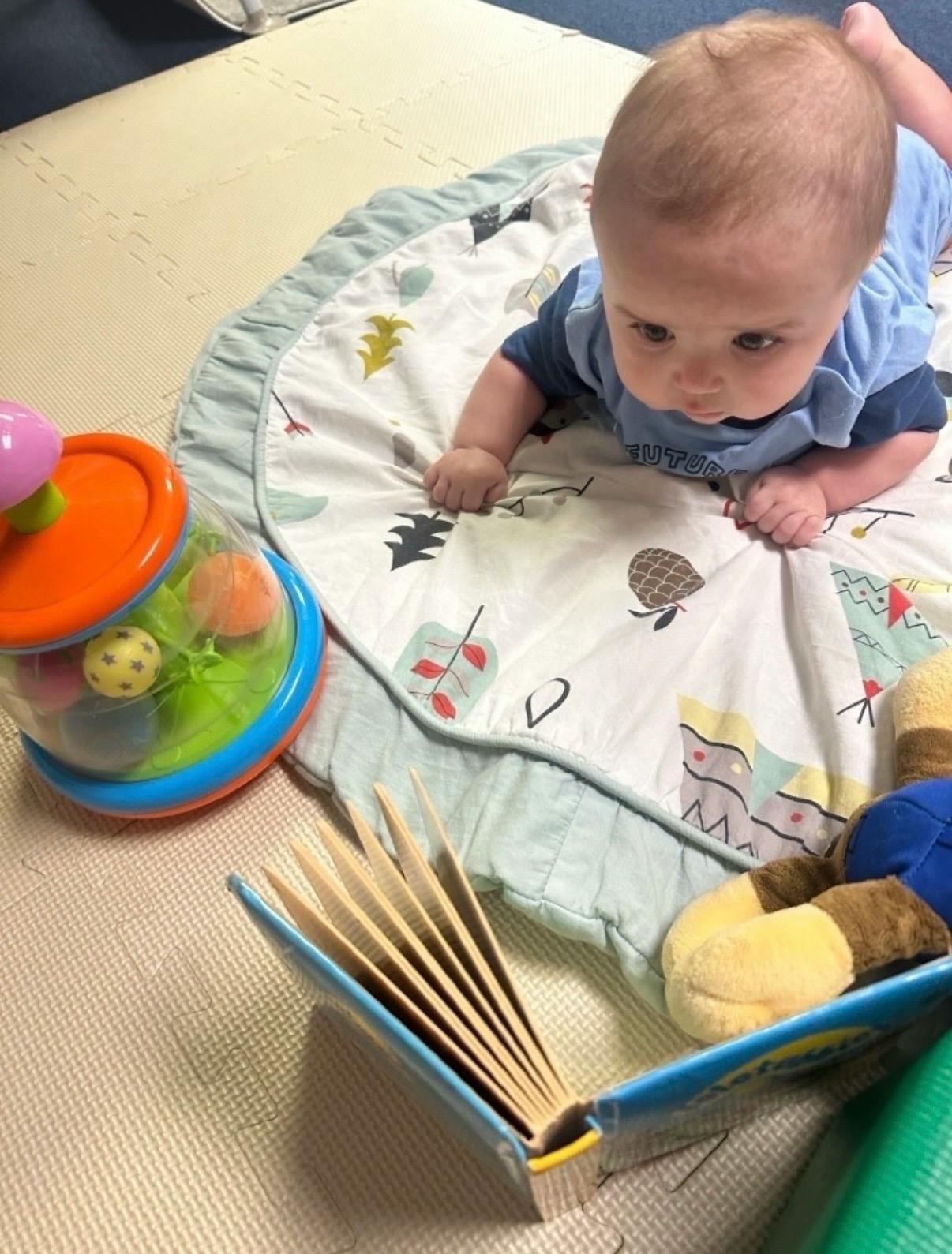 Baby lying on a play mat with toys and a book