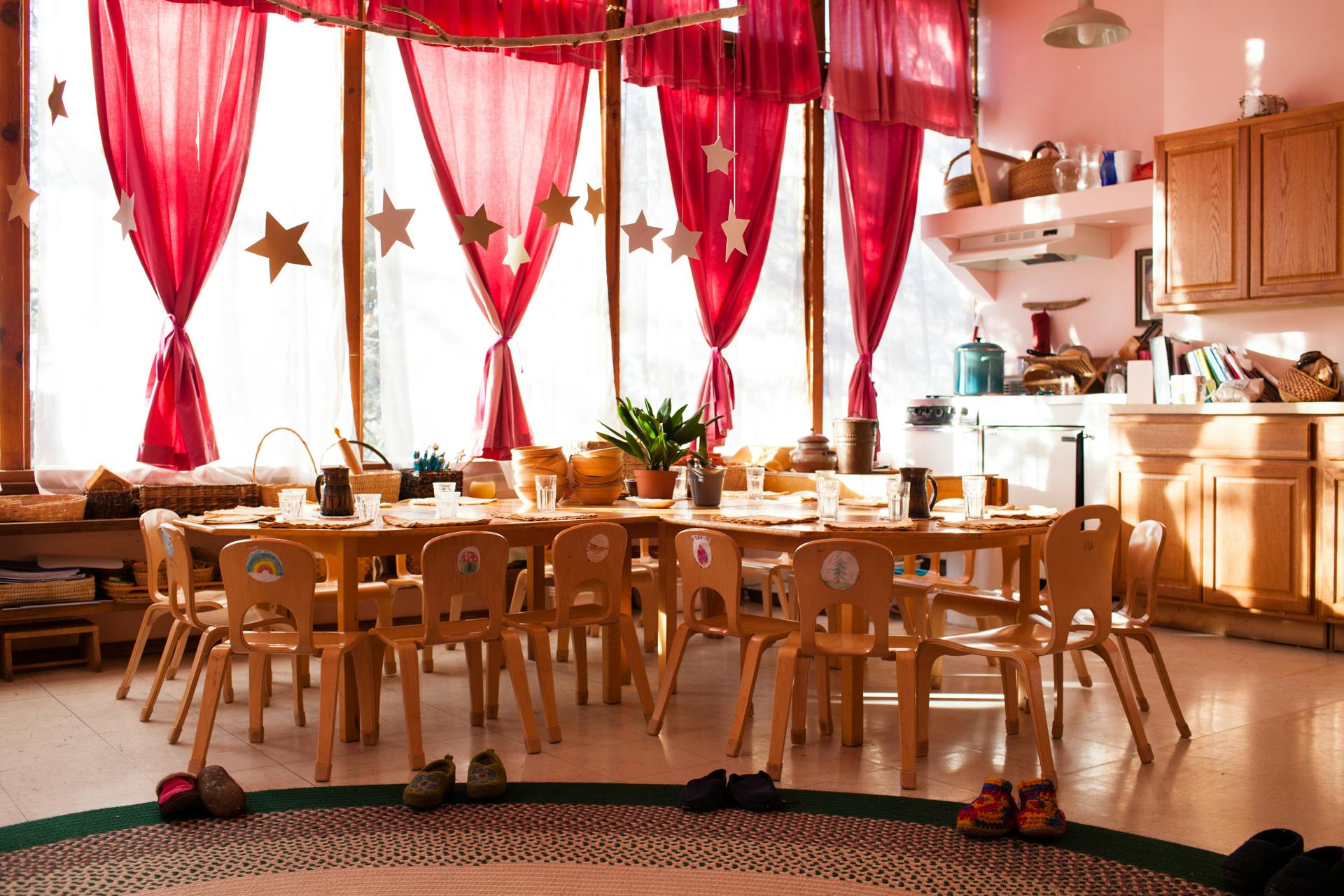 Classroom with small tables and chairs, red curtains, and a kitchen area
