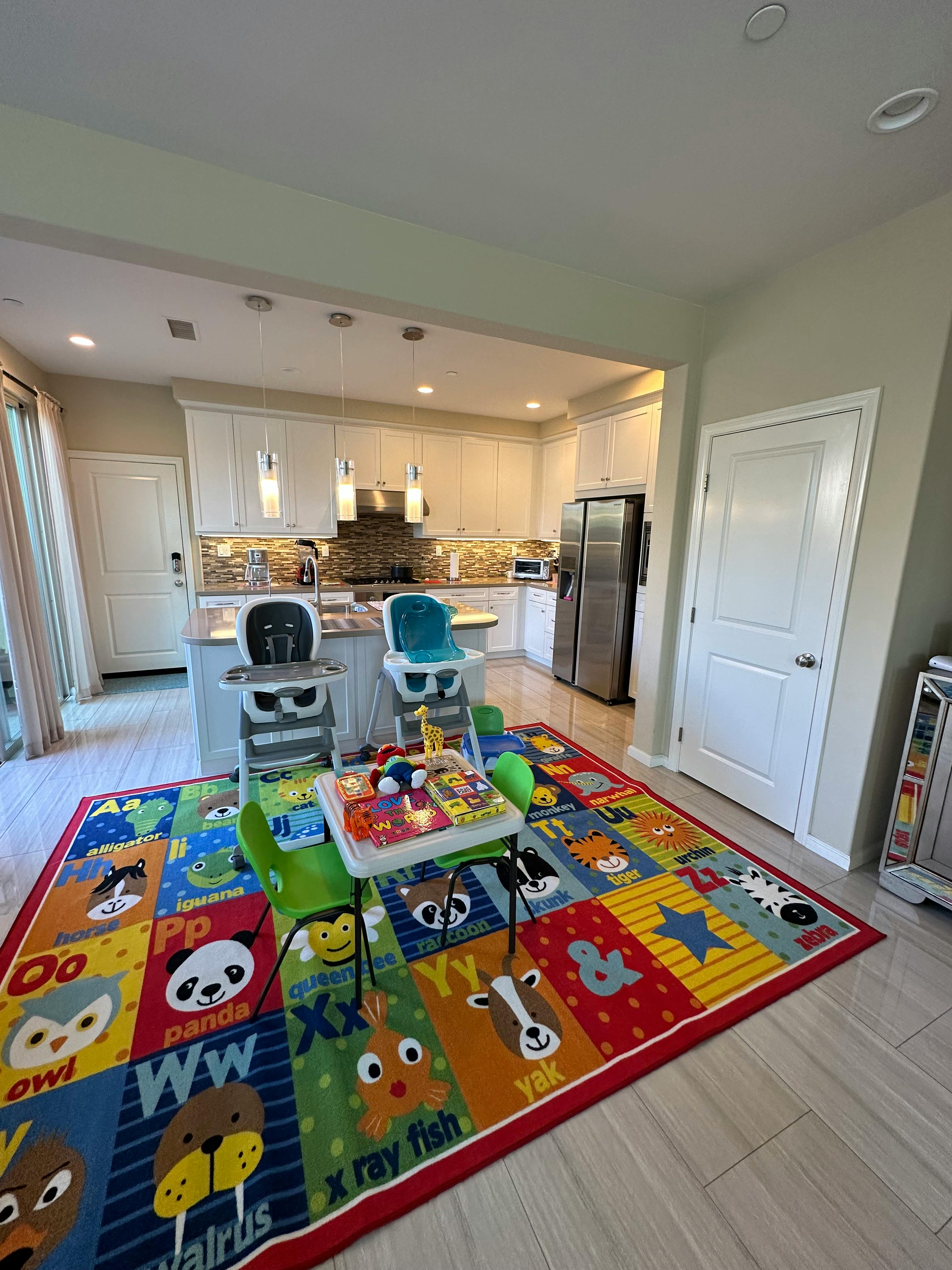 Two high chairs and a child's play table on an alphabet rug in a kitchen