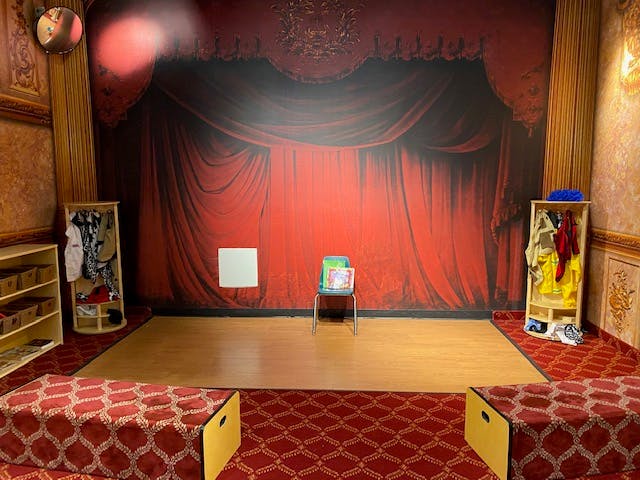 Room with red curtain backdrop, wooden floor, and red patterned carpet