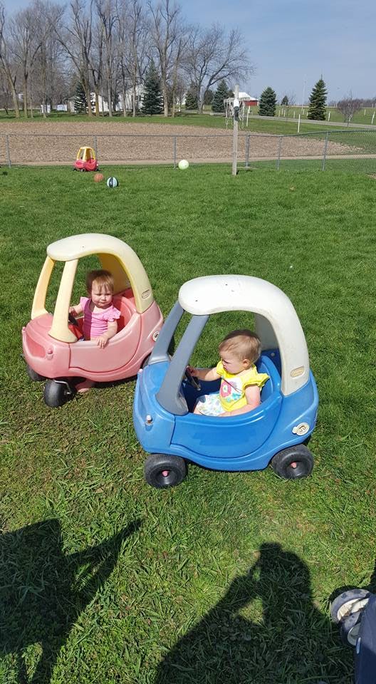 Two children in toy cars on grass