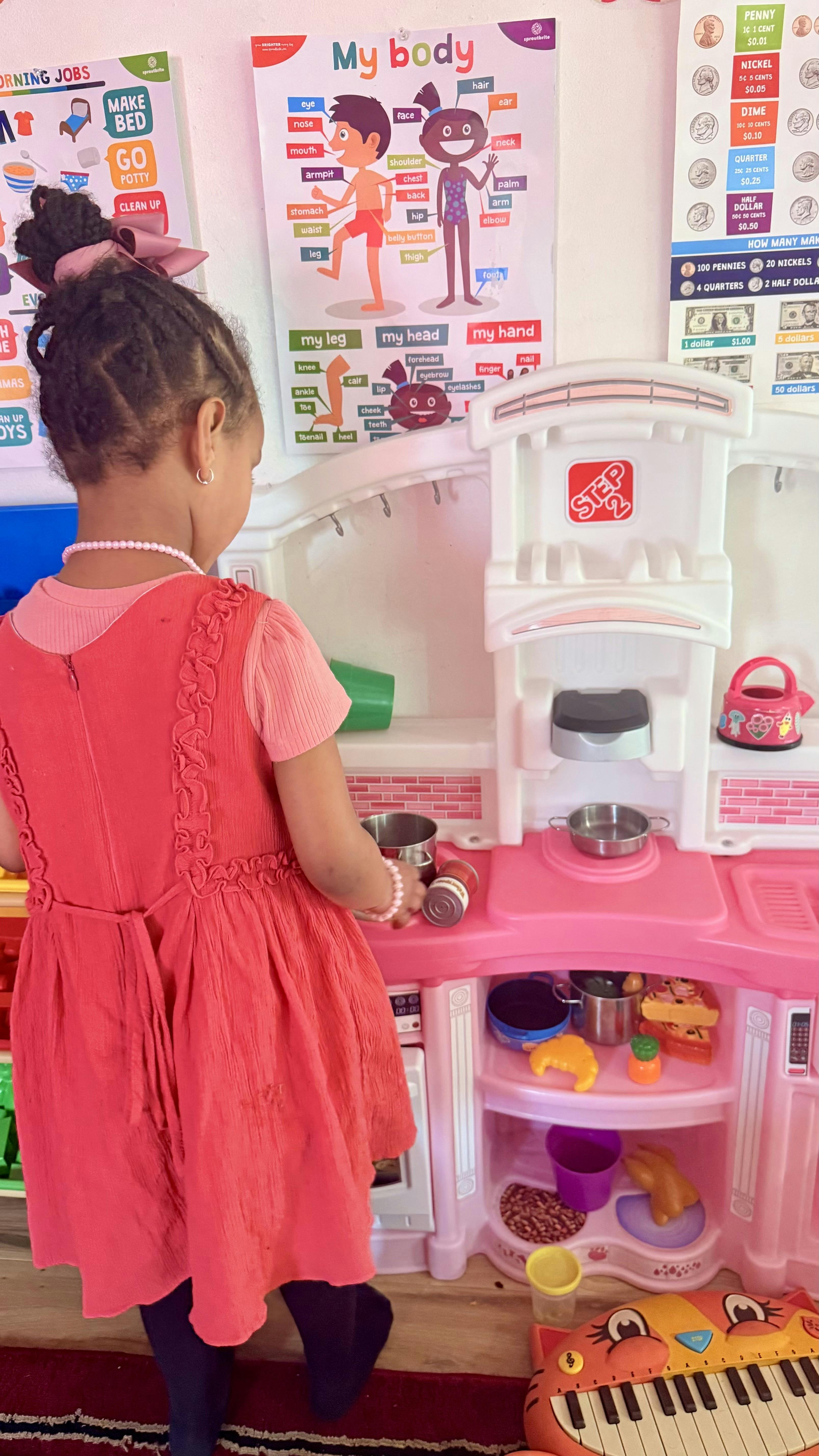 Child playing at a pink toy kitchen set