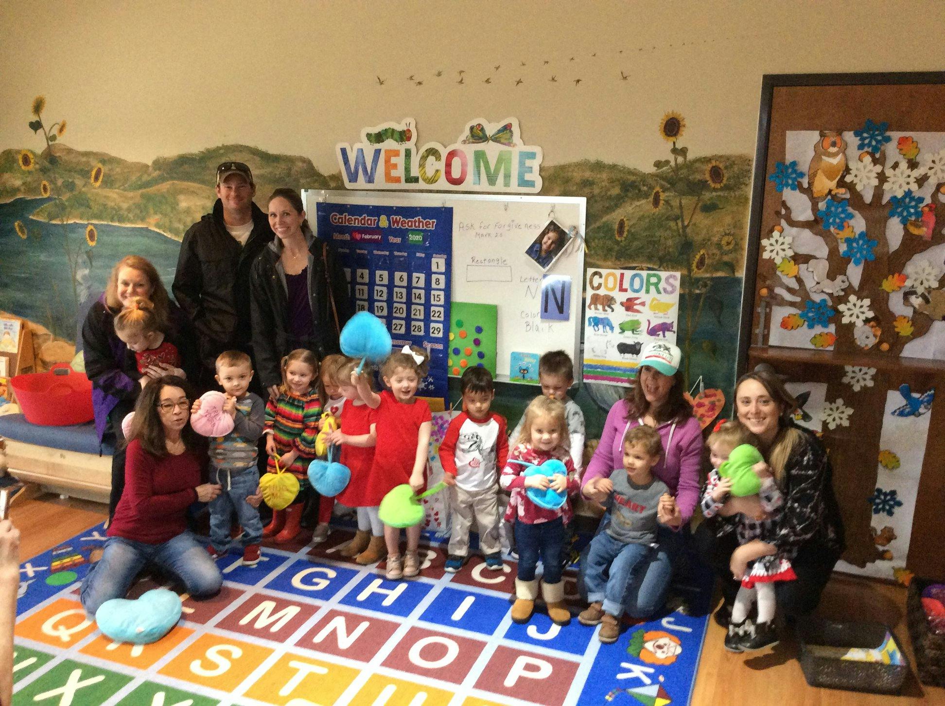 Group of adults and children in a classroom with a "WELCOME" sign
