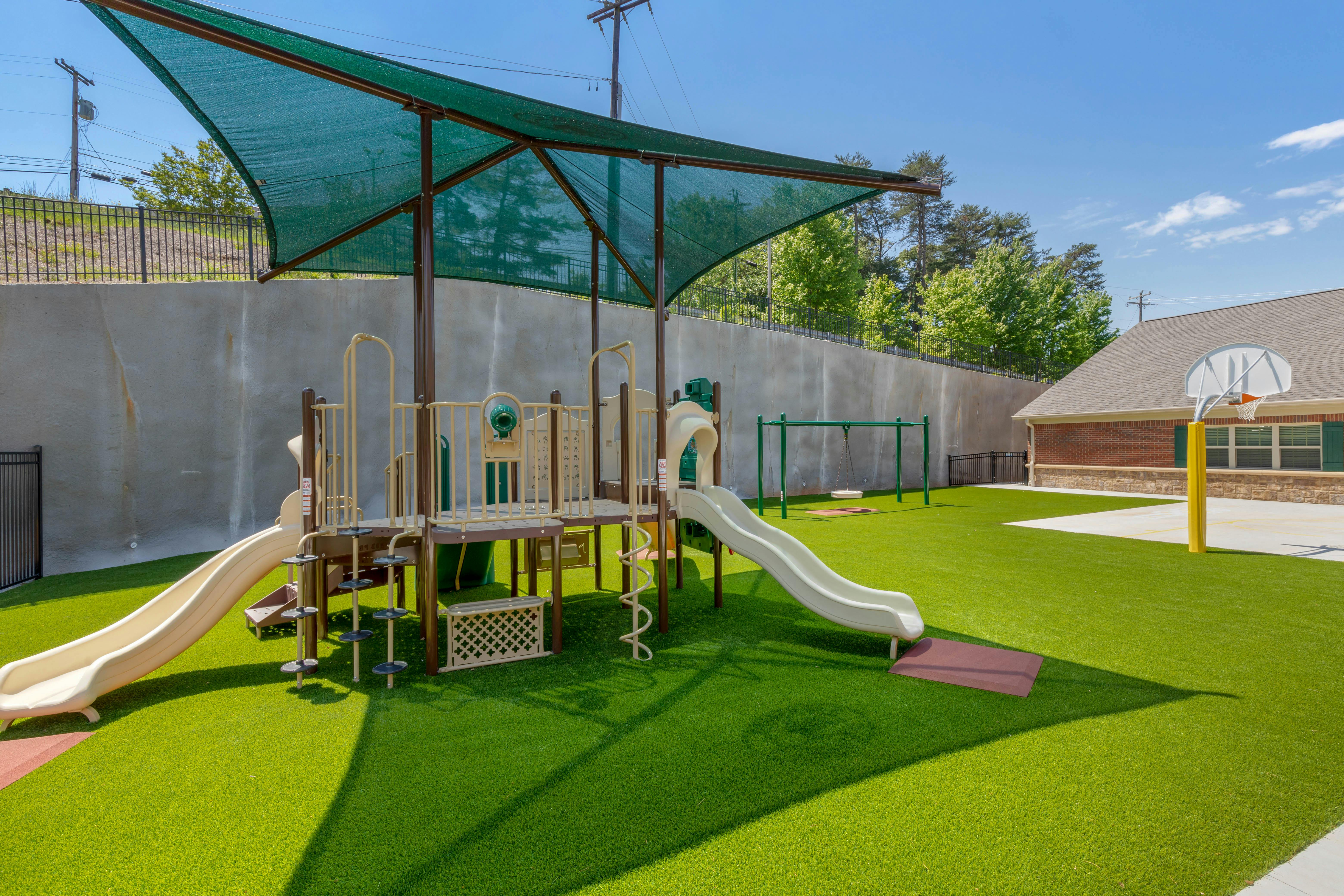 Outdoor playground with artificial turf, play structure, swings, and basketball hoop