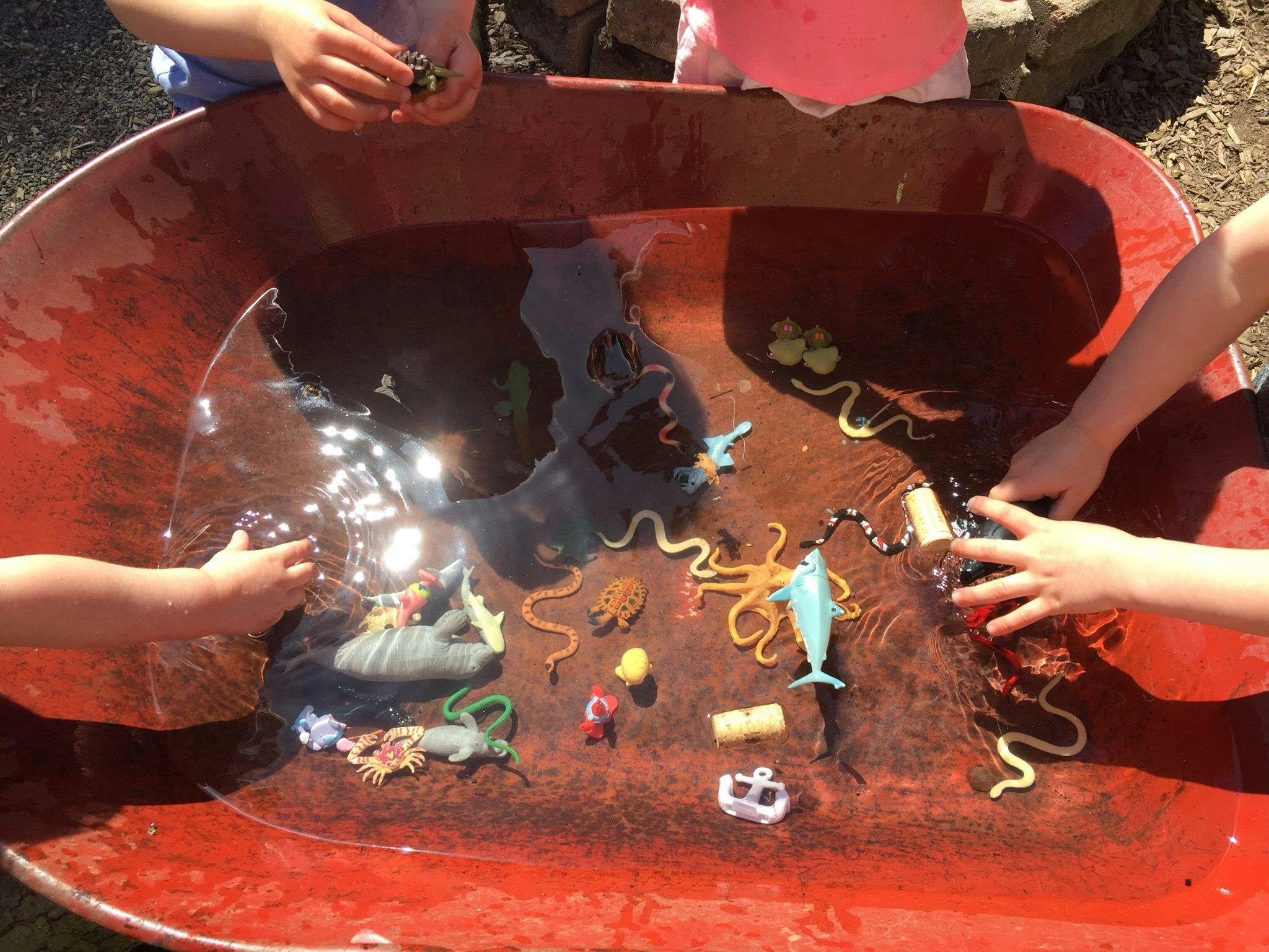 Children playing with animal toys in a red tub of water