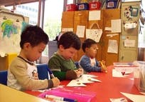 Three children drawing at a table in a classroom