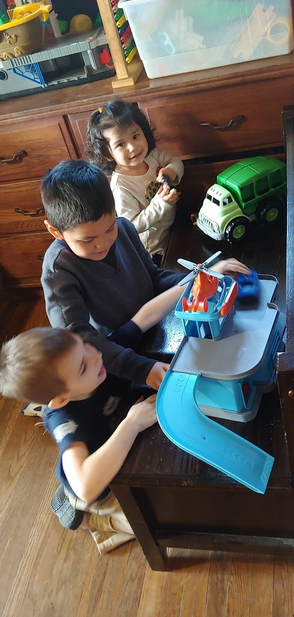 Three children playing with toys on a wooden floor