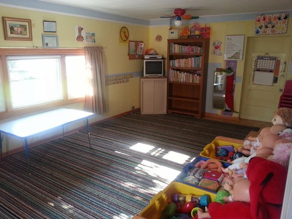 Room with a table by a window, a bookshelf, and toys in a bin