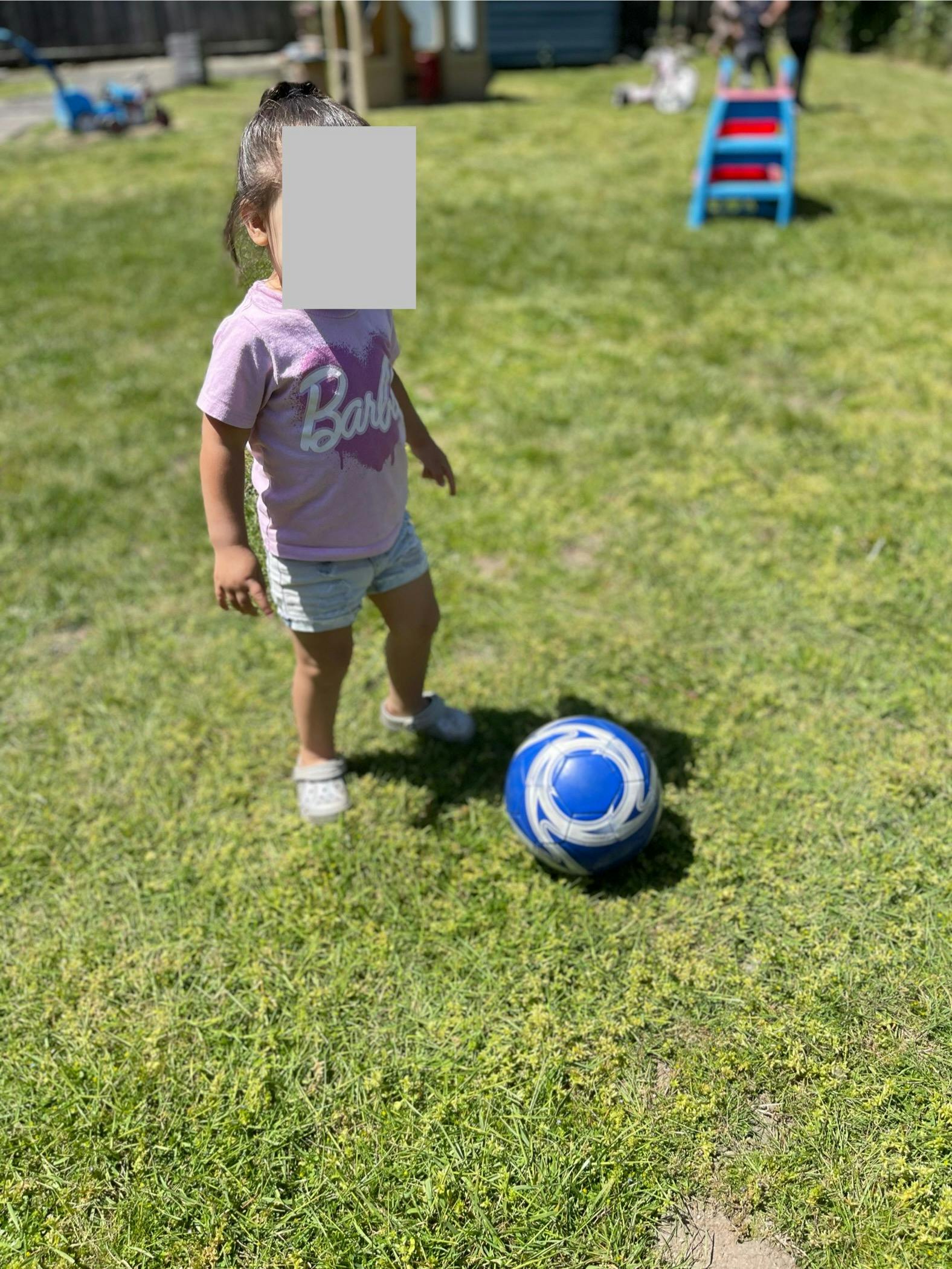 Child standing on grass next to a blue and white ball