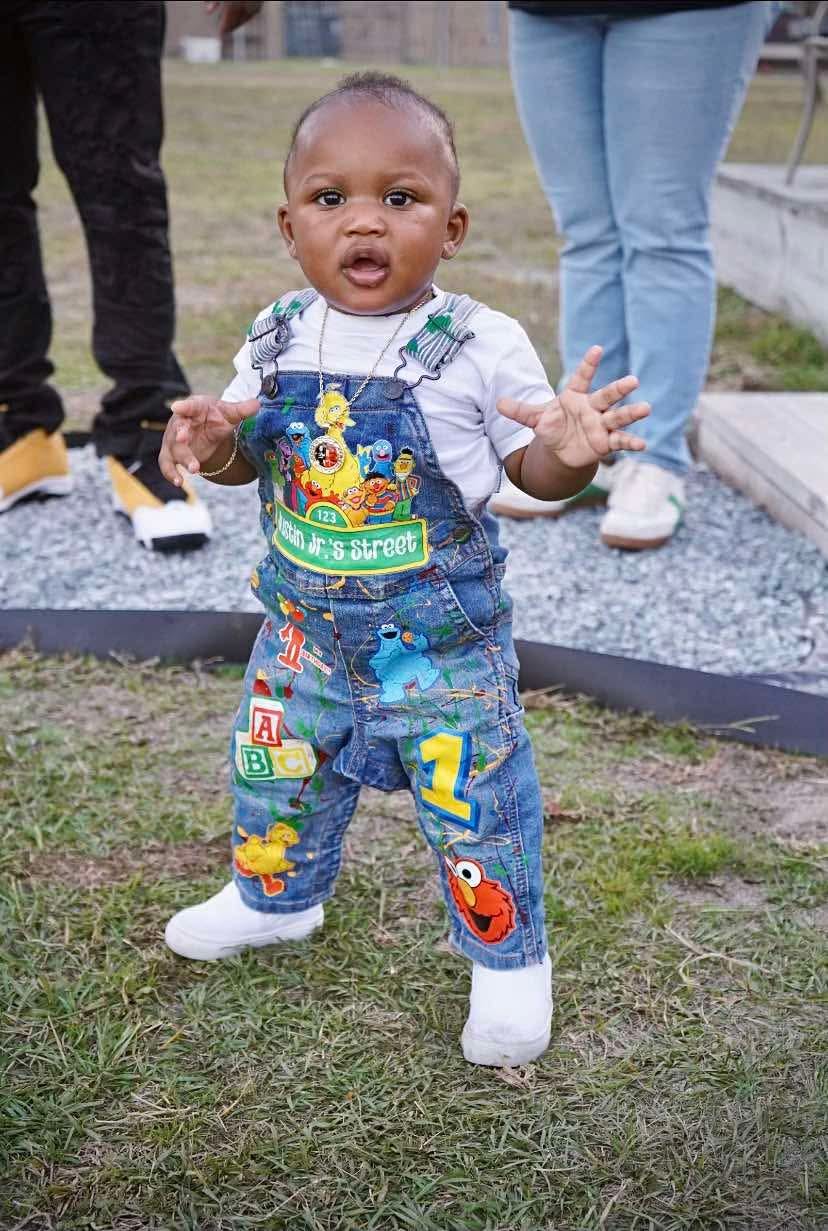Child in denim overalls with Sesame Street characters standing on grass