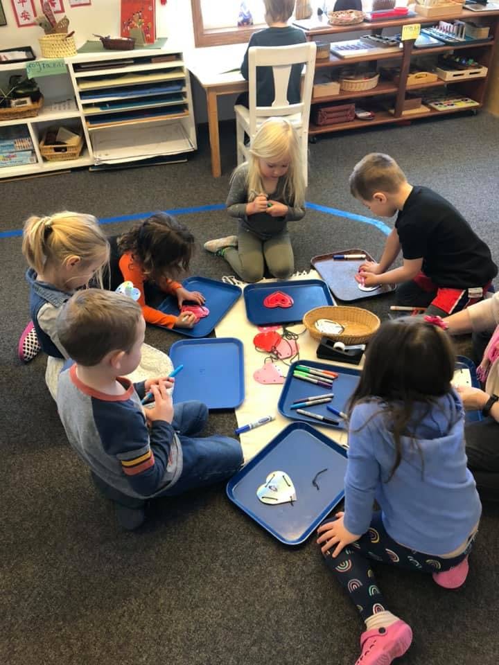 Children sitting on the floor around trays with art supplies
