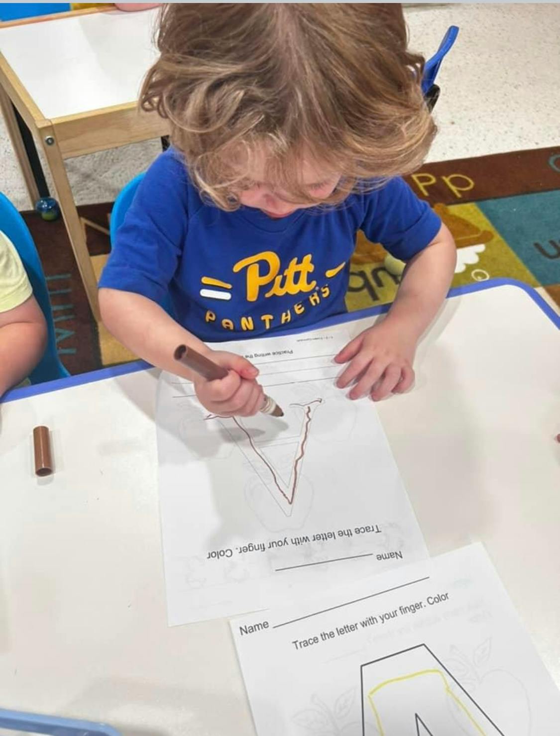 Child tracing a letter on a worksheet with a marker