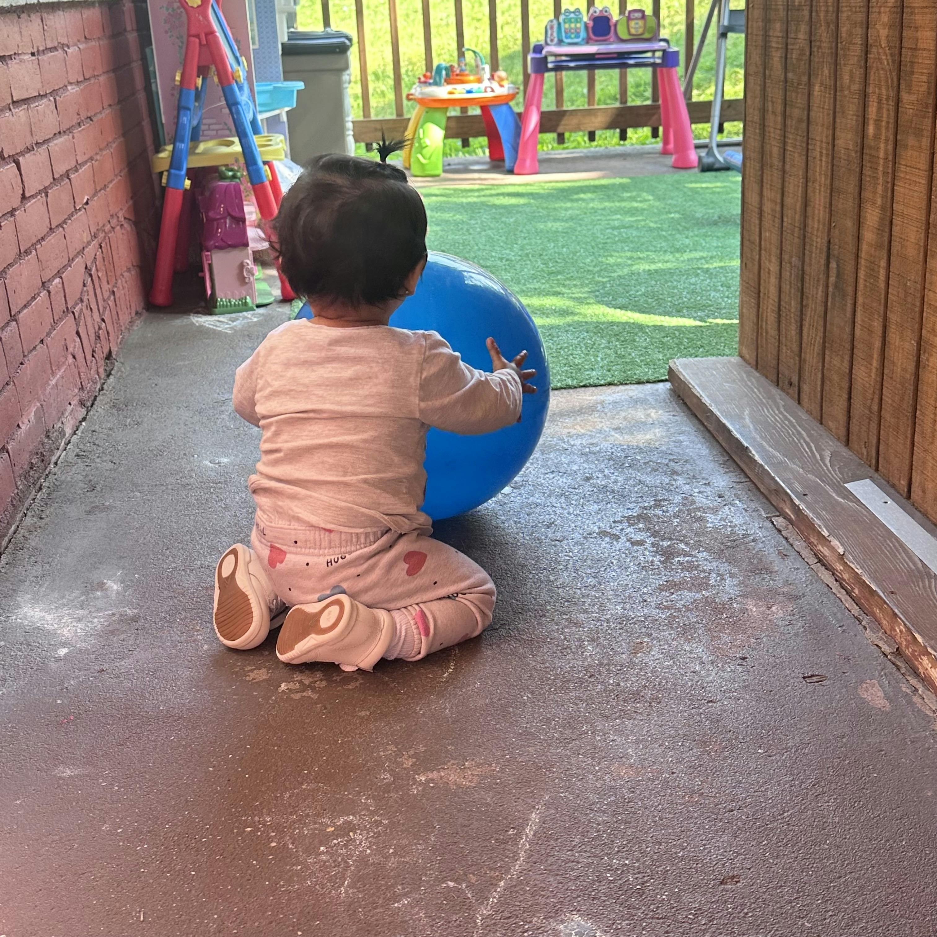 Child on hands and knees pushing a blue ball