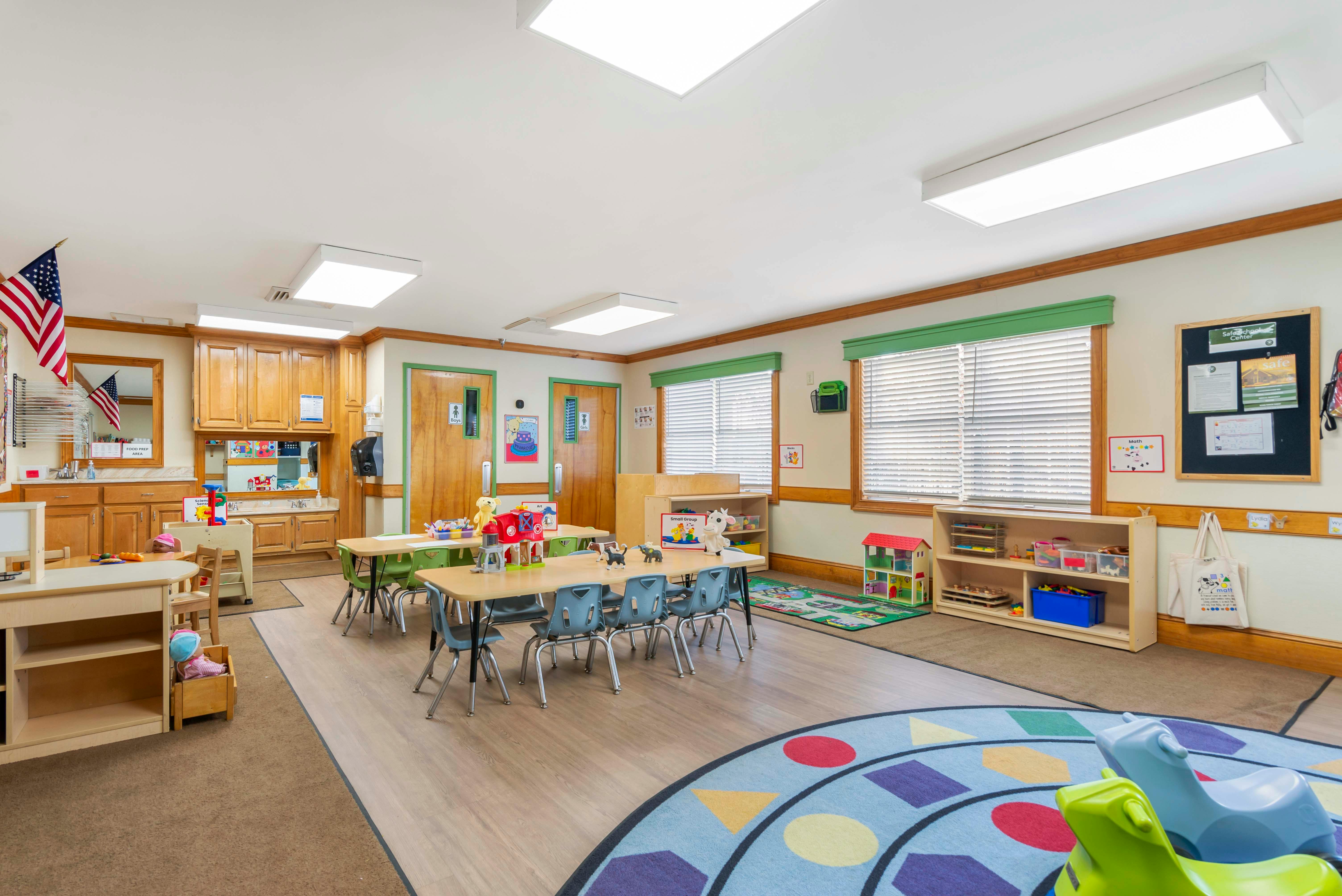 Classroom with tables, chairs, play areas, and an American flag